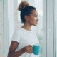A person holding a mug and looking out a bright window in morning light, representing the quiet reckoning that often follows drinking to manage anxiety