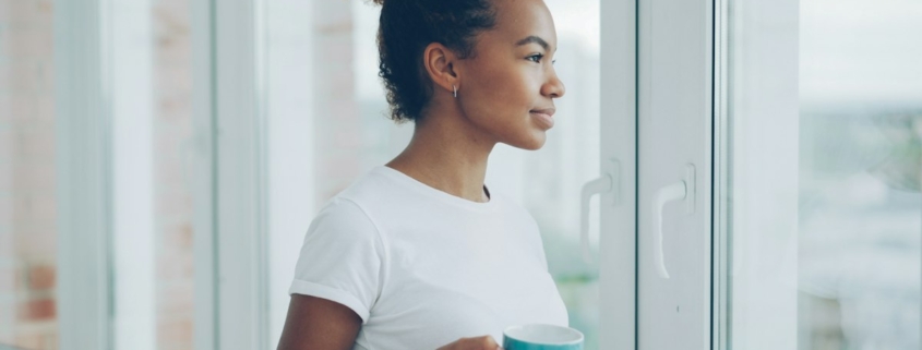 A person holding a mug and looking out a bright window in morning light, representing the quiet reckoning that often follows drinking to manage anxiety