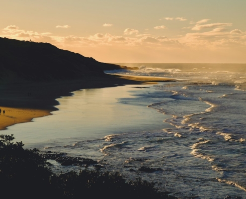 Two people walking along a quiet beach at sunset, a calm image of small daily activity