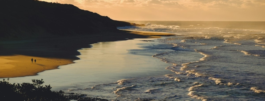 Two people walking along a quiet beach at sunset, a calm image of small daily activity