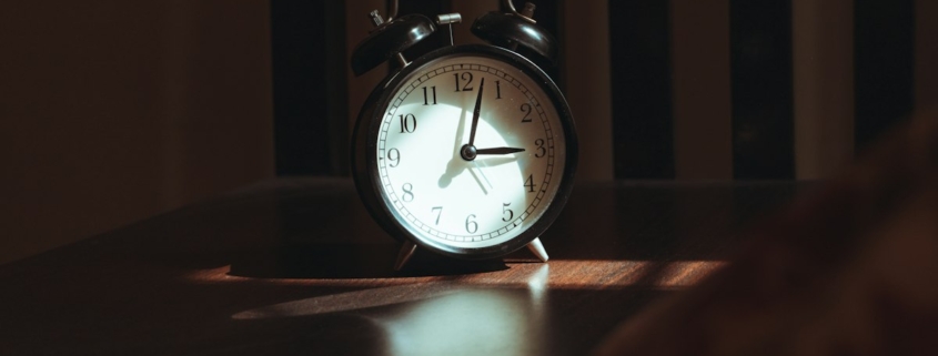 A classic alarm clock on a bedside table in soft light, representing the steady sleep and daily routine that support bipolar disorder stabilization