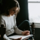Woman sitting in a chair by a window writing in a notebook, keeping a daily mood log