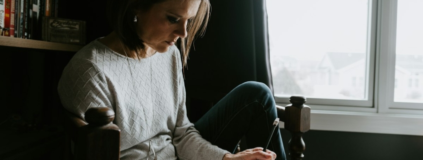 Woman sitting in a chair by a window writing in a notebook, keeping a daily mood log