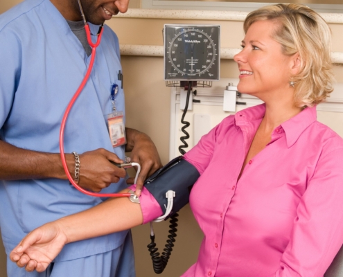 Healthcare worker in scrubs checking a patient blood pressure in a clinic