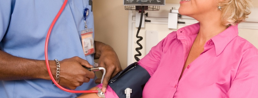 Healthcare worker in scrubs checking a patient blood pressure in a clinic