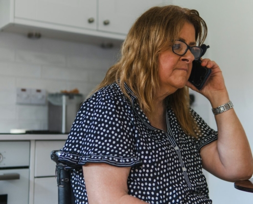 A woman sitting at her kitchen table making a phone call with a concerned expression