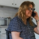 A woman sitting at her kitchen table making a phone call with a concerned expression