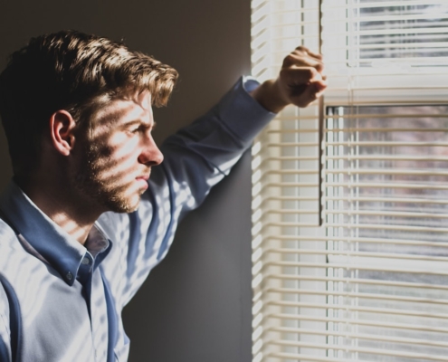 Person standing at a window in soft daylight, considering which level of mental health care to pursue