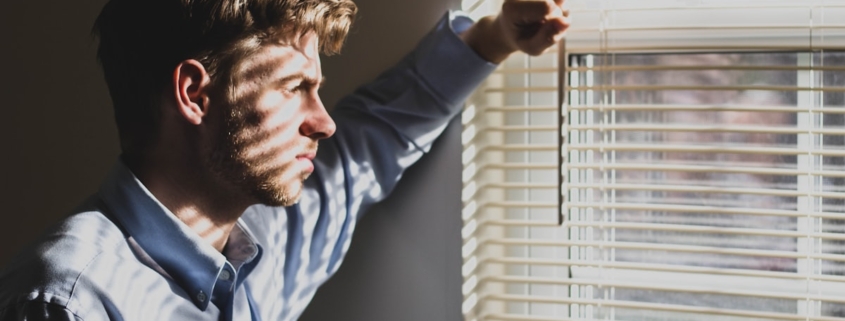 Person standing at a window in soft daylight, considering which level of mental health care to pursue