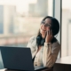A woman smiling as she takes a phone call at a desk by a bright window