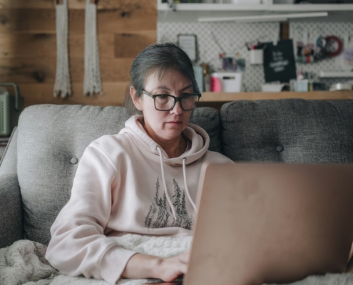 Woman sitting on a couch at home researching mental health treatment options on a laptop