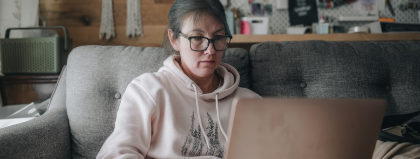 Woman sitting on a couch at home researching mental health treatment options on a laptop