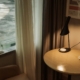 A quiet sunlit corner with an armchair, a small round table, a lamp and a cup beside a curtained window