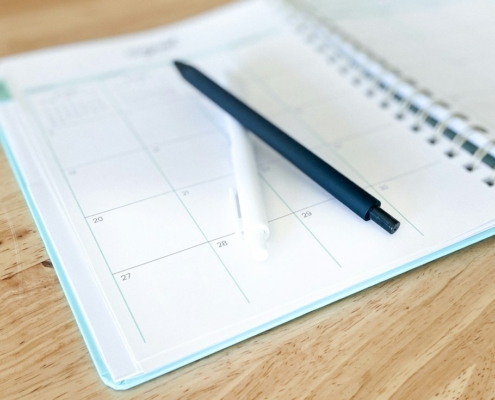 Open monthly planner with two pens on a wooden table, used to track insurance authorization and review dates