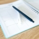 Open monthly planner with two pens on a wooden table, used to track insurance authorization and review dates