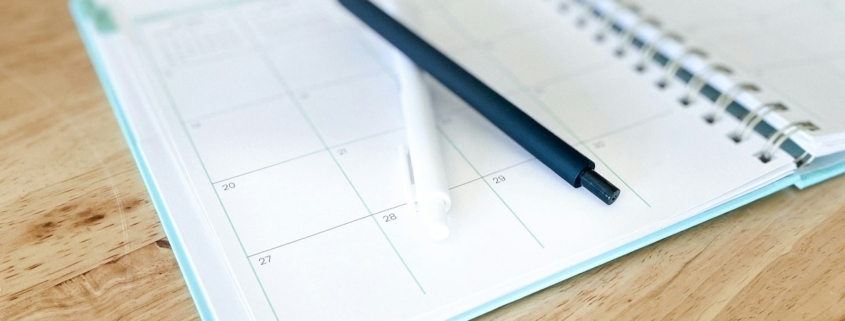 Open monthly planner with two pens on a wooden table, used to track insurance authorization and review dates