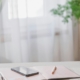 Open planner, pen and phone on a bright table by a sheer-curtained window with green plants, a calm setting for preparing questions before calling a treatment program