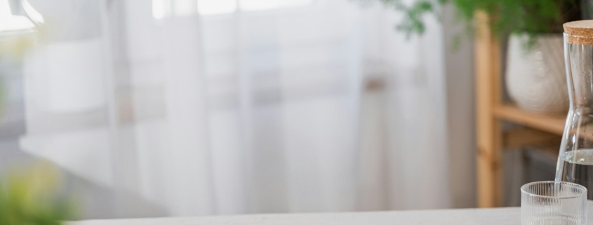 Open planner, pen and phone on a bright table by a sheer-curtained window with green plants, a calm setting for preparing questions before calling a treatment program