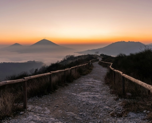 A fenced gravel path leading toward misty mountains at sunrise