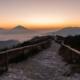 A fenced gravel path leading toward misty mountains at sunrise