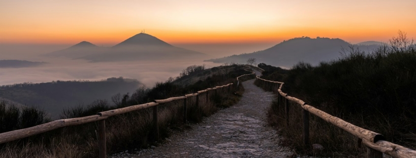 A fenced gravel path leading toward misty mountains at sunrise