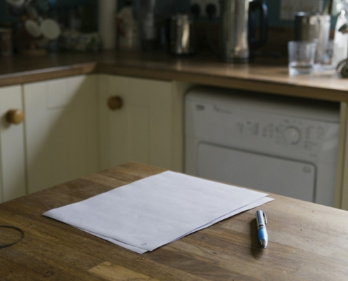 Sheets of paper and a pen on a wooden kitchen table, ready for writing down a medication history