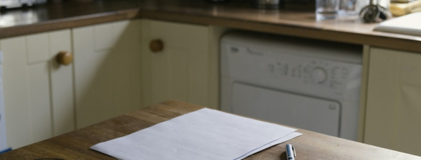 Sheets of paper and a pen on a wooden kitchen table, ready for writing down a medication history