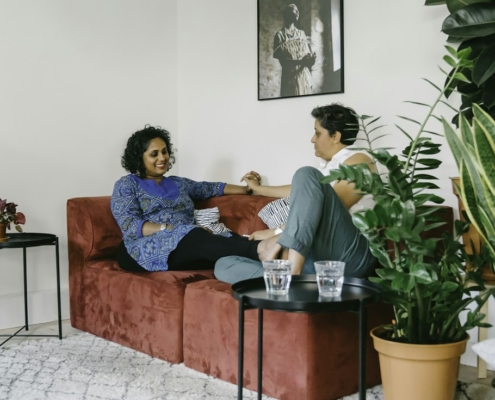Two people sitting on a couch in a bright living room having a calm, unhurried conversation.