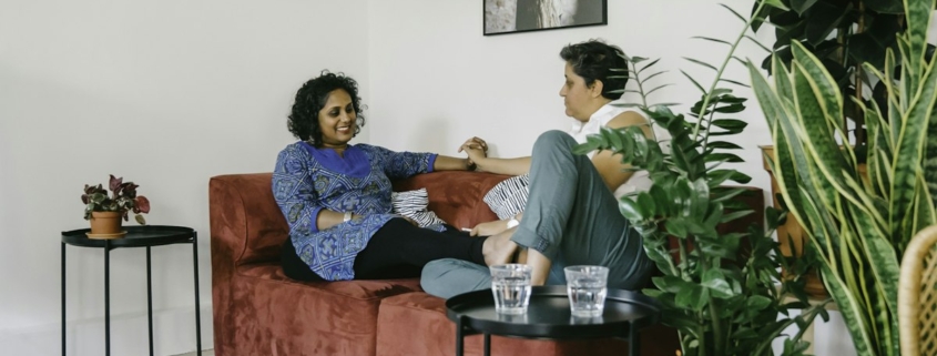 Two people sitting on a couch in a bright living room having a calm, unhurried conversation.
