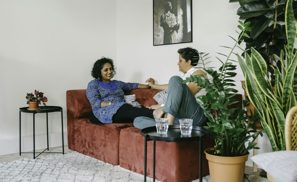 Two people sitting on a couch in a bright living room having a calm, unhurried conversation.