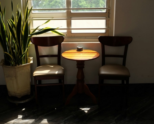 Two wooden chairs and a small round table beside a sunlit window, a calm setting for a conversation at home