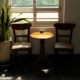Two wooden chairs and a small round table beside a sunlit window, a calm setting for a conversation at home