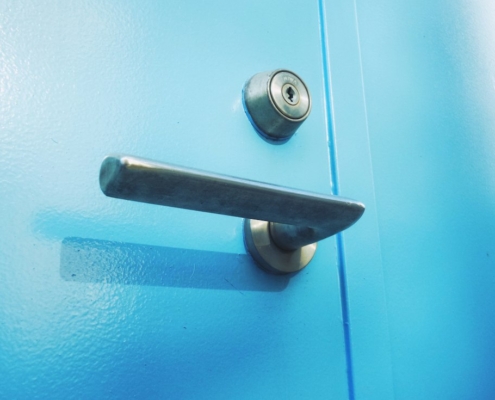 Close-up of a door lever and deadbolt lock on a bright blue door, representing checking compulsions addressed in exposure and response prevention for OCD