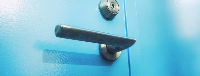 Close-up of a door lever and deadbolt lock on a bright blue door, representing checking compulsions addressed in exposure and response prevention for OCD