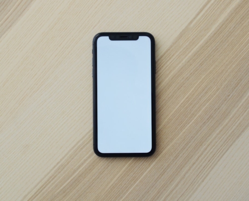 A plain black smartphone with a blank screen lying on a light wooden table