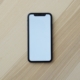 A plain black smartphone with a blank screen lying on a light wooden table