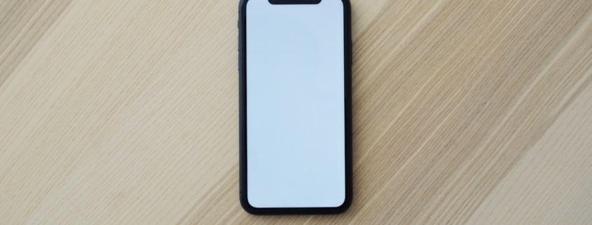A plain black smartphone with a blank screen lying on a light wooden table