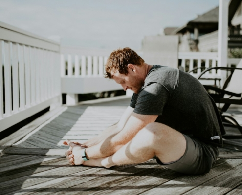A man doing a seated forward stretch on a sunlit wooden porch, illustrating gentle physical activity during residential mental health treatment