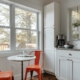 A sunlit kitchen with a small round table and two empty chairs beside a large window