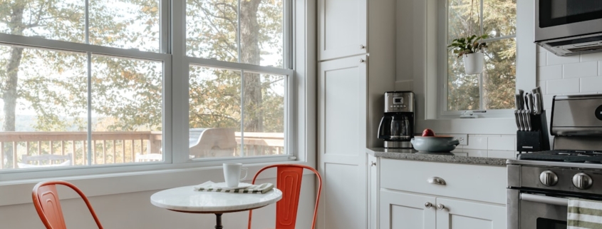 A sunlit kitchen with a small round table and two empty chairs beside a large window