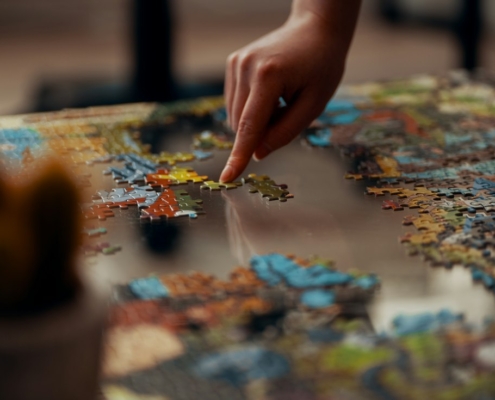 A hand placing a piece in a colorful jigsaw puzzle on a table, representing how psychological testing helps assemble a clearer clinical picture