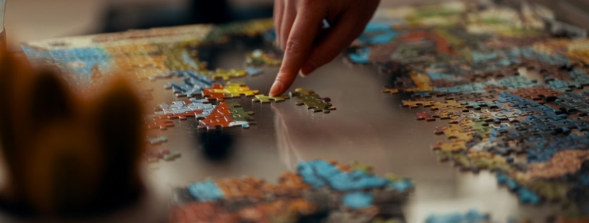 A hand placing a piece in a colorful jigsaw puzzle on a table, representing how psychological testing helps assemble a clearer clinical picture