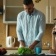 Woman on a phone call taking notes at a kitchen counter while her partner prepares a salad
