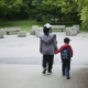A parent and young child walk hand in hand along a tree-lined park path