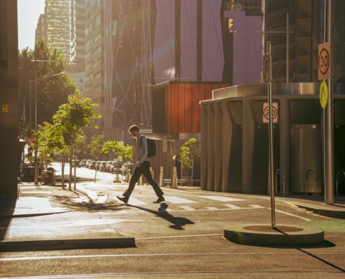 A person with a backpack walking across a quiet city street in early morning light on the way to work