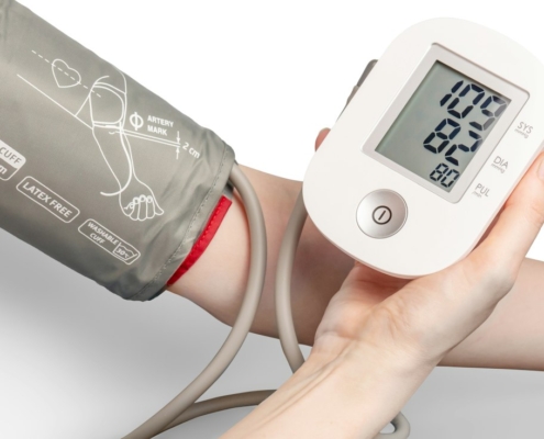 A blood pressure cuff on an adult arm with a digital monitor held in one hand, part of a routine physical exam