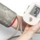 A blood pressure cuff on an adult arm with a digital monitor held in one hand, part of a routine physical exam