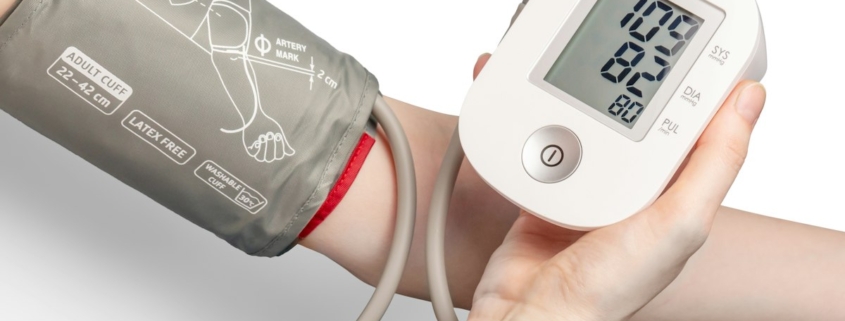 A blood pressure cuff on an adult arm with a digital monitor held in one hand, part of a routine physical exam