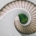 A bright white spiral staircase seen from above, curving inward toward green plants growing at its center.