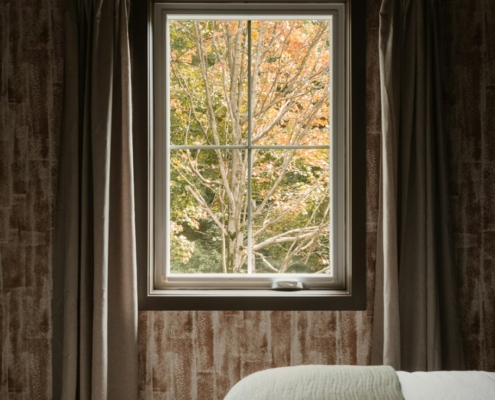 Soft daylight through a bedroom window framing autumn trees with orange and green leaves